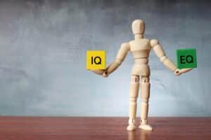 Hölzerne menschliche Figur balanciert Holzklötze mit der Aufschrift IQ und EQ.