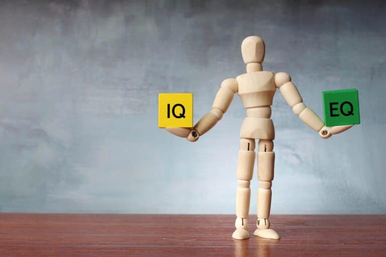 Hölzerne menschliche Figur balanciert Holzklötze mit der Aufschrift IQ und EQ.